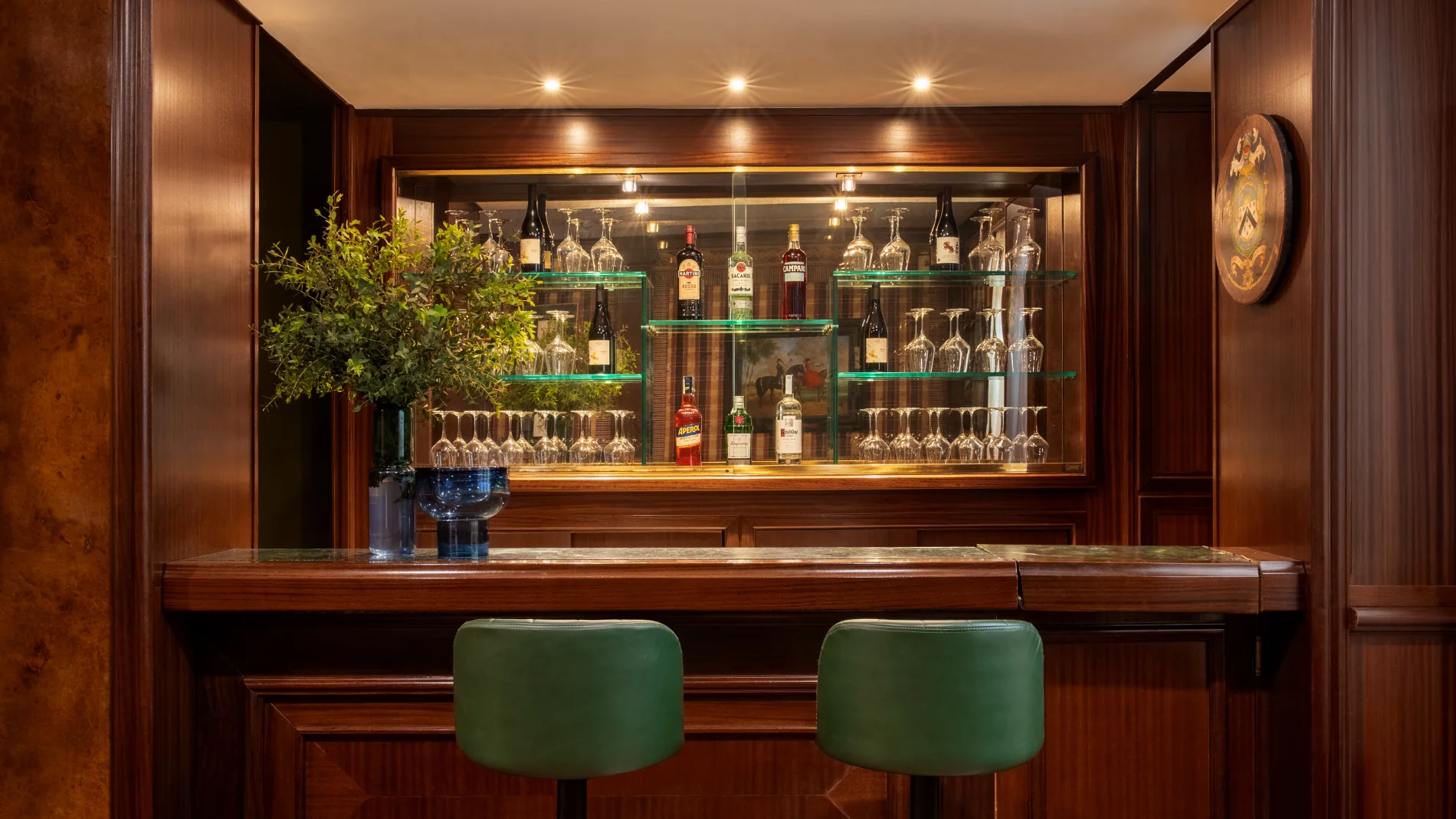 Angolo bar in legno con sgabelli verdi, vetrina illuminata, bottiglie e calici nel centro di Roma - The Hotel Britannia, BZAR hotels a Roma