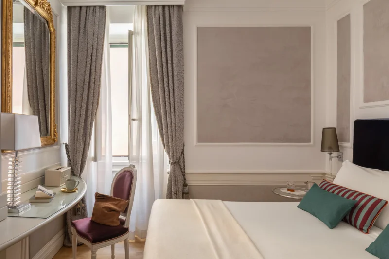 Camera Deluxe luminosa con letto matrimoniale, specchio dorato, scrittoio e tende grigie nel centro di Roma - The Hotel Britannia, BZAR hotels a Roma