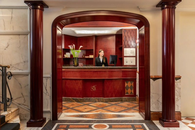 Reception elegante con banco rosso, colonne in legno, marmi e staff vicino a Piazza della Repubblica - The Hotel Britannia, BZAR hotels a Roma