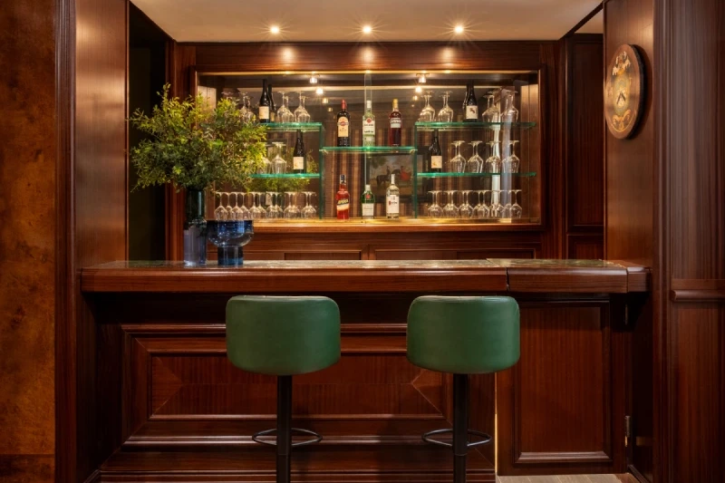 Angolo bar in legno con sgabelli verdi, bottiglie, calici e vetrina illuminata nel centro di Roma - The Hotel Britannia, BZAR hotels a Roma
